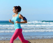 Frau joggt am Meer mit Smartphone