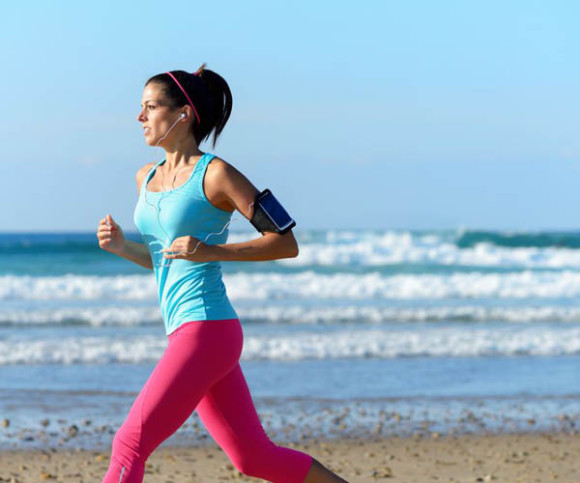 Frau joggt am Meer mit Smartphone 